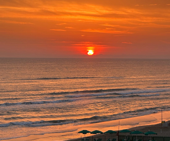 Delegare la vendita per costruire liberta imprenditoriale: tramonto arancione su una spiaggia con ombrelloni verdi