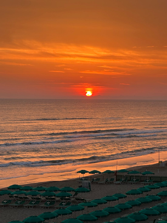 Delegare la vendita per costruire liberta imprenditoriale: tramonto arancione su una spiaggia con ombrelloni verdi